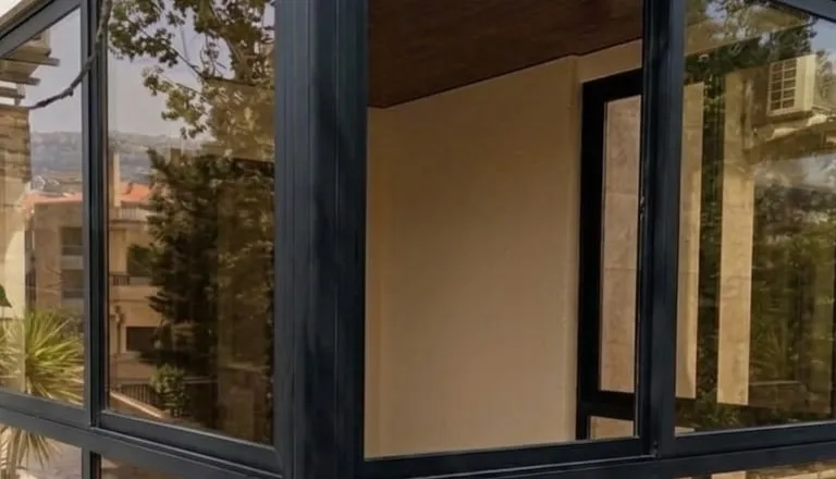 Black aluminium corner glazing reflecting garden trees