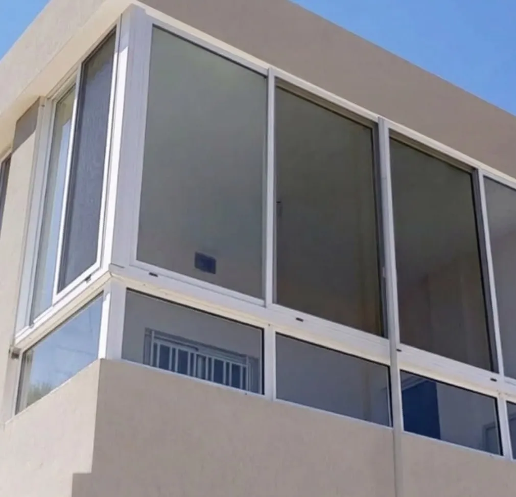 White aluminium corner enclosure with double-glazed sliding panels on a rendered facade